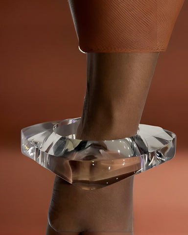 Close-up of the Orbitz Round Lucite Bangle by Nik Spruill on a person's wrist against a brown background. The person is wearing a textured brown sleeve, adding an air of understated luxury.