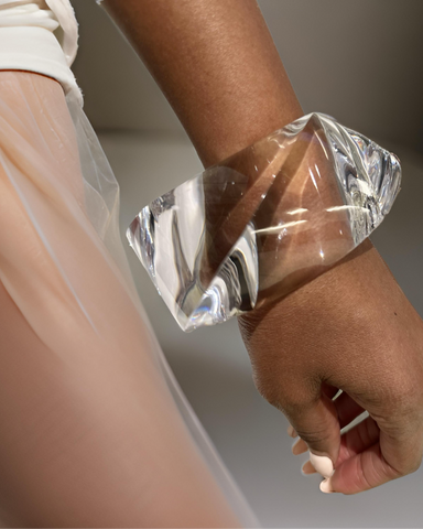 Close-up of a person wearing the Nik Spruill Liquid Lucite Asymmetrical Bangle Bracelet on their wrist, with part of a sheer, light-colored garment visible.