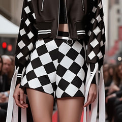 A person strolls down the city street in a striking black and white CHECKMATE CROCHET SHORT by Nik Spruill, featuring a color block design and ribbon details that add an extra flair of style.