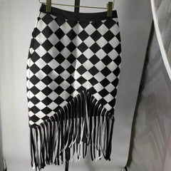 Discover the Nik Spruill Checkmate Crochet Fringe Skirt—a stylish black and white checkered piece with a fringed hem. Crafted with a crochet interlock technique and color block design, it's elegantly showcased on a hanger.