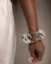 A close-up of a person's arm wearing the Swirl Liquid Lucite Cuff Bracelet by Nik Spruill. The person has dark skin and is dressed in a light-colored garment.