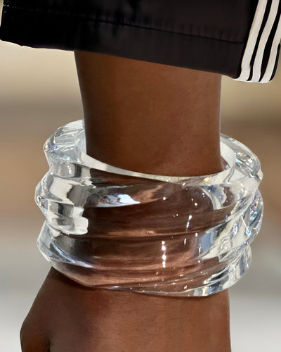 A close-up image displays a hand-sculpted, clear, textured Nik Spruill Liquid Lucite Wave Cuff Bracelet gracing the wrist of a person, showcasing a modern piece.
