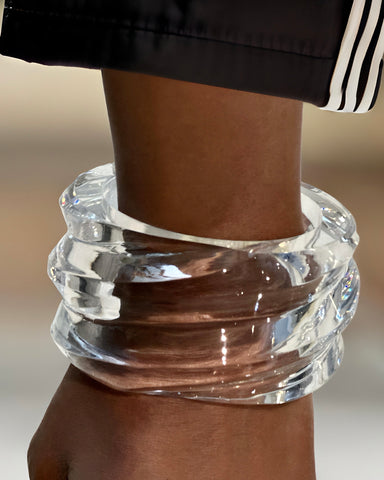 A close-up image displays a hand-sculpted, clear, textured Nik Spruill Liquid Lucite Wave Cuff Bracelet gracing the wrist of a person, showcasing a modern piece.