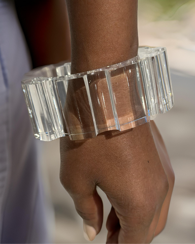A hand wearing a large, transparent, rectangular-shaped Nik Spruill Geer Lucite Cuff Bracelet showcases a modern design.