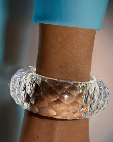 A clear, textured Croc Lucite Cuff Bracelet by Nik Spruill graces a wrist against a light blue background, highlighting an elegant fashion accessory.