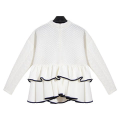 The CrossRoads Top by Nik Spruill is a white textured blouse featuring a peplum design with navy blue hem trim, long sleeves, and a 3D laser-cut pattern that blends classic style and modern flair. Made-to-order for exclusivity.