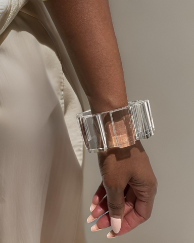 A person wearing a translucent, rectangular Geer Lucite Cuff Bracelet by Nik Spruill on their wrist and a beige fabric garment.