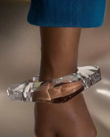 A person's arm, ornamented with a Nik Spruill Orbitz Round Lucite Bangle, is shown against a neutral background. The person is dressed in a blue textured sleeve.