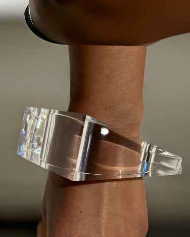 A person wears the Liquid Lucite Wedge Bangle Bracelet by Nik Spruill, a clear, handcrafted bangle with a geometric design made from transparent material.