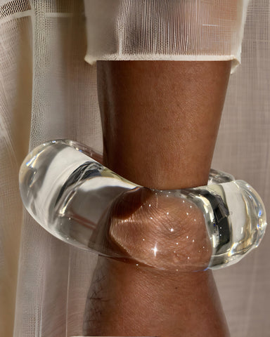 Close-up view of a person's arm wearing a thick, hand-polished Lucite Stackable Circle Bangle Bracelet by Nik Spruill, with a sheer fabric background.