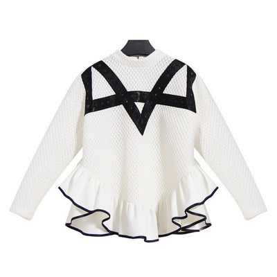 The Nik Spruill Crossroads Top is a made-to-order white sweater featuring long sleeves, black v-shaped detailing, and a ruffled hem.