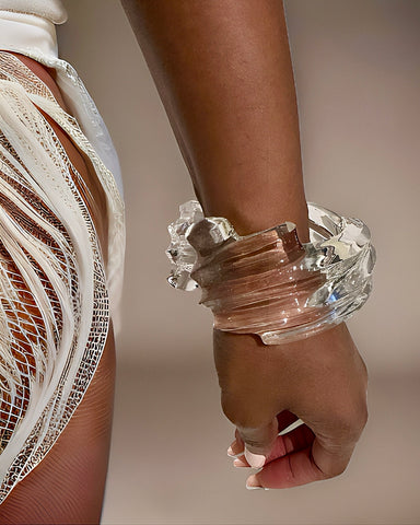 Close-up of a person wearing a Nik Spruill Spiral Liquid Lucite Cuff Bracelet and a white fringed garment, featuring an eye-catching cascading wave detail.