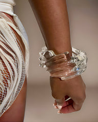 Close-up of a person wearing a Nik Spruill Spiral Liquid Lucite Cuff Bracelet and a white fringed garment, featuring an eye-catching cascading wave detail.