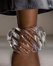 Close-up of a person wearing the large, transparent Nik Spruill Wiggle Lucite Cuff Bracelet with unique twisted details on their wrist, with part of a dark skirt or dress visible above.
