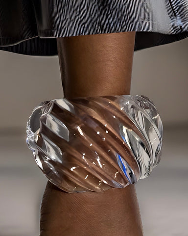 Close-up of a person wearing the large, transparent Nik Spruill Wiggle Lucite Cuff Bracelet with unique twisted details on their wrist, with part of a dark skirt or dress visible above.