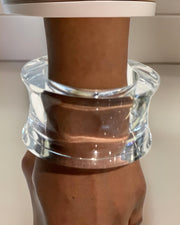 A clear, wide, cylindrical bracelet from Nik Spruill is worn on a wrist, creating the illusion of the wrist being encased in the timeless Dream Rain Lucite Cuff Bracelet with sophisticated design.