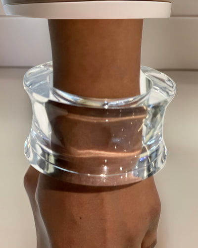 A clear, wide, cylindrical bracelet from Nik Spruill is worn on a wrist, creating the illusion of the wrist being encased in the timeless Dream Rain Lucite Cuff Bracelet with sophisticated design.