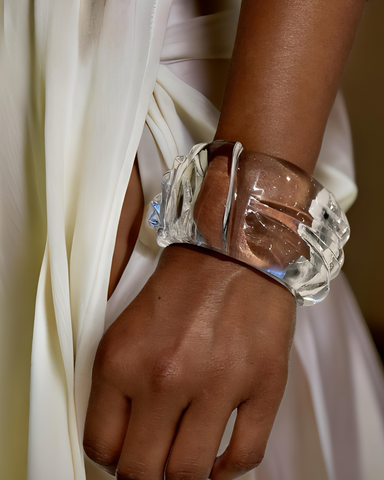 A close-up of a person wearing the Bow Lucite Cuff Bracelet by Nik Spruill on their wrist. They are dressed in a white, flowing garment.