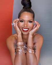 A person with a styled updo and bright smile poses against a divided red and gray background, wearing a Luminous Lucite Cuff Bangle Bracelet by Nik Spruill.