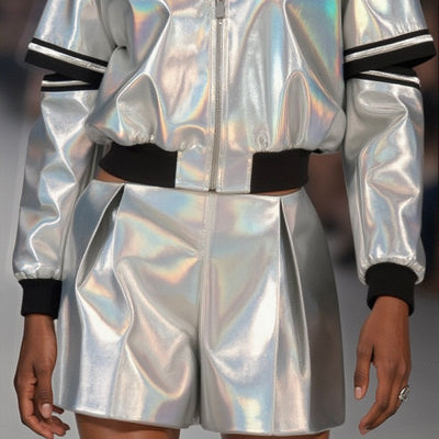 A person is wearing an ILLUMINATE SHORT by Nik Spruill, featuring silver metallic fabric with shiny, iridescent details and black cuffs.