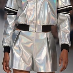A person is wearing an ILLUMINATE SHORT by Nik Spruill, featuring silver metallic fabric with shiny, iridescent details and black cuffs.