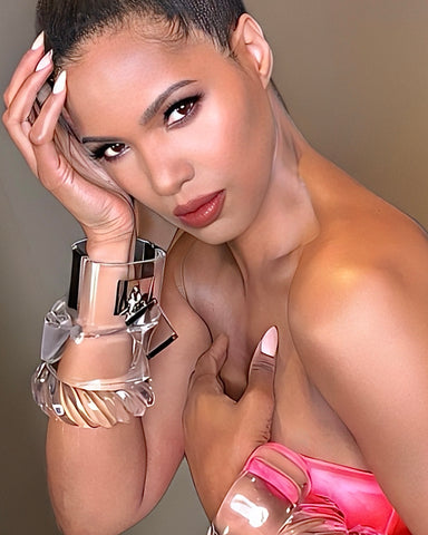 A person with styled hair, wearing a pink strapless top and a Nik Spruill Drop Lock Silver Lucite Bangle Bracelet, poses elegantly with one hand on their face and the other on their chest.