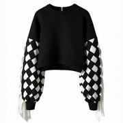 The Stitch Crochet Fringed Top by Nik Spruill is a striking black sweatshirt with unique ribbon interlock white and black sleeves. The ribbon hangs like fringe creating a unique look. Front view