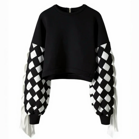 The Stitch Crochet Fringed Top by Nik Spruill is a striking black sweatshirt with unique ribbon interlock white and black sleeves. The ribbon hangs like fringe creating a unique look. Front view