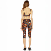 Woman wearing a black and orange patterned sports bra and leggings set on a white background