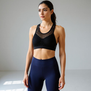 Woman wearing a black sports bra and navy leggings against a gray background