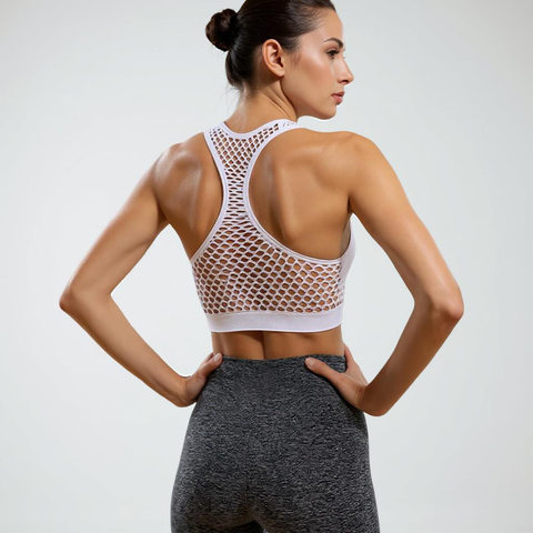Woman wearing a white mesh sports bra and gray leggings on a plain background