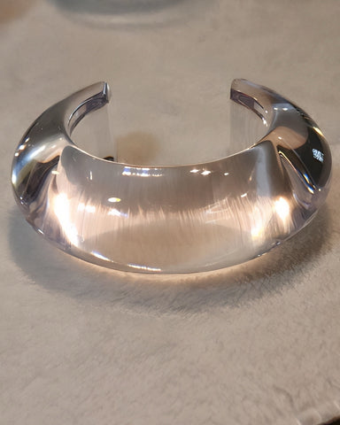 The ARCTIC by Nik Spruill, a hand-polished clear acrylic cuff bracelet, rests on a light-colored surface, showcasing its elegant curves and refined simplicity.