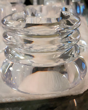 A close-up of a clear glass ashtray with a stacked, ribbed design, placed on a white napkin, reminiscent of the intricate detailing seen in hand-carved Arctic clear Lucite cuff bracelets by Nik Spruill.