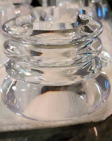 A close-up of a clear glass ashtray with a stacked, ribbed design, placed on a white napkin, reminiscent of the intricate detailing seen in hand-carved Arctic clear Lucite cuff bracelets by Nik Spruill.