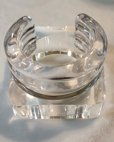 The ICEBERG clear, chunky Lucite bangle bracelet by Nik Spruill rests elegantly atop a square, transparent glass block.