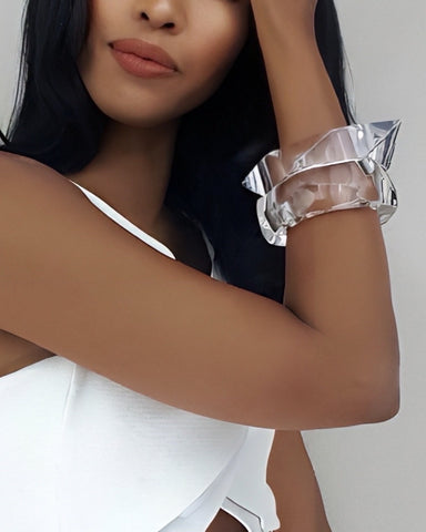 A person with long dark hair wears Nik Spruill's white GLOSS sleeveless top and a large clear bangle while posing with an arm resting on their head.