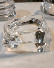 A close-up of two stacked, ICICLE hand-carved, transparent glass bracelets by Nik Spruill, placed on a white surface.