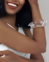 A person wearing a white sleeveless top, smiling, and holding their left arm up to reveal the ICICLE clear lucite bracelet by Nik Spruill on their wrist.