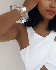 Close-up of a person with dark hair and smooth skin, wearing a white sleeveless top and showcasing the OHSO large, hand-carved silver bracelet by Nik Spruill, holding their hand near their head.
