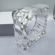 A METROPOLIS Carved Lucite cube sculpture by Nik Spruill, featuring an intricate design and a hollow center, placed on a reflective surface with a white background.
