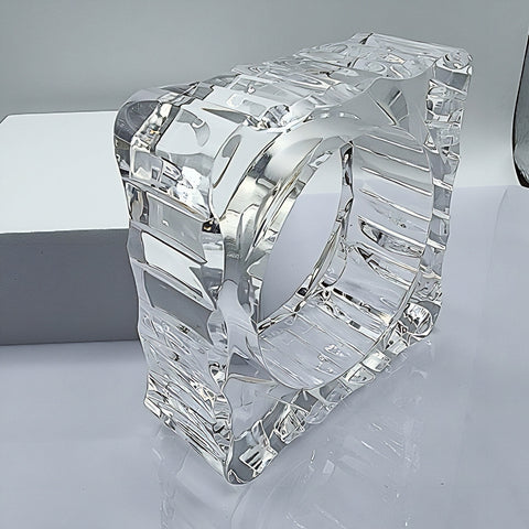A METROPOLIS Carved Lucite cube sculpture by Nik Spruill, featuring an intricate design and a hollow center, placed on a reflective surface with a white background.
