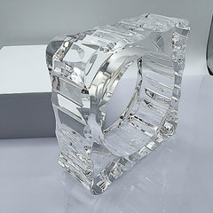A METROPOLIS Carved Lucite cube sculpture by Nik Spruill, featuring an intricate design and a hollow center, placed on a reflective surface with a white background.