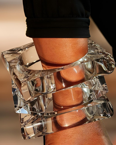 Close-up of a person's forearm adorned with the Nik Spruill Glaze Lucite Bangle Bracelets featuring large, geometric, clear designs. They are dressed in a black sleeve.