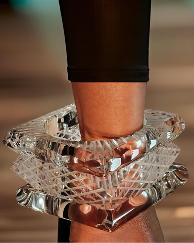 A wrist adorned with the Frost Lucite Bangle Bracelets by Nik Spruill, featuring large, intricately cut, transparent crystal bracelets with distinctive etched detailing.