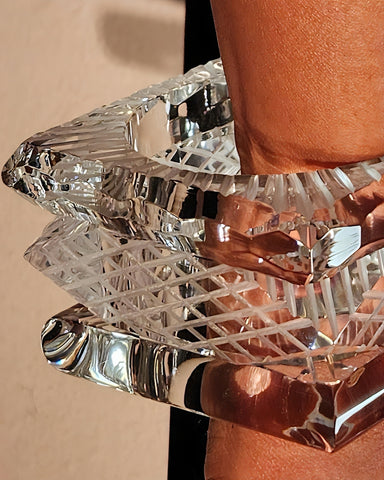 Close-up of a person's arm wearing a transparent, intricately cut Frost Lucite Bangle Bracelet by Nik Spruill with distinctive etched detailing against a light background.