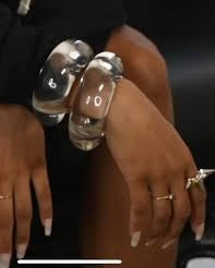 A person wearing a Nik Spruill Bubble Lucite Cuff Bracelet and several rings rests their hand on their knee.