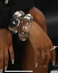 A person wearing a Nik Spruill Bubble Lucite Cuff Bracelet and several rings rests their hand on their knee.