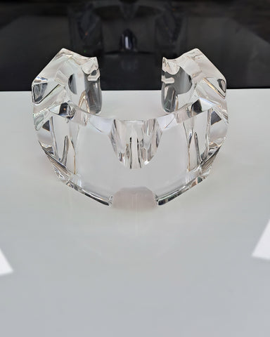 A clear, intricately-cut Liquid Lucite Infinity Cuff Bracelet by Nik Spruill is displayed on a reflective surface.