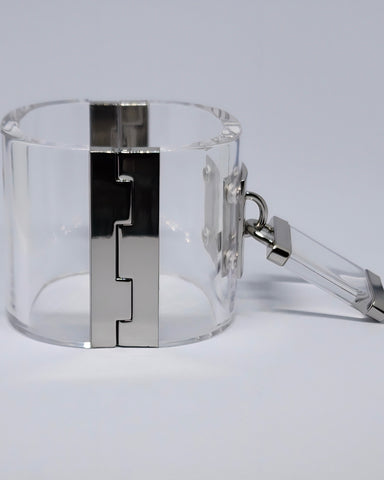 Embrace sophistication with the Drop Lock Silver Lucite Bangle Bracelet by Nik Spruill, featuring a sleek cylindrical design in clear Lucite. It includes a silver metallic hinge, square clasp, and a petite key attached by chain. The magnetic closure ensures easy wear while preserving its chic allure.