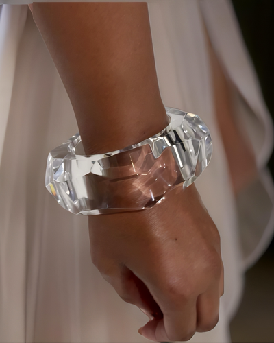 A person wearing an elegant, thick Angles Lucite Bangle Bracelet by Nik Spruill on their wrist. They are dressed in a white, flowy garment, adding to the unique accessory's allure.